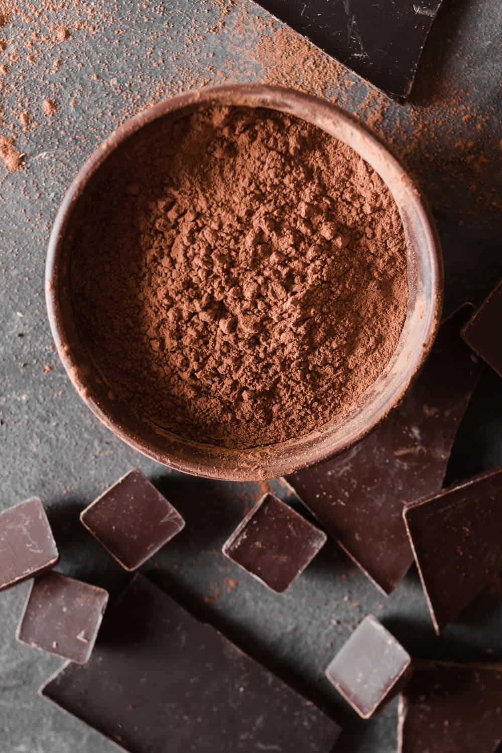 Schokoladenstückchen und Kakaopulver auf grauem abstraktem Hintergrund.