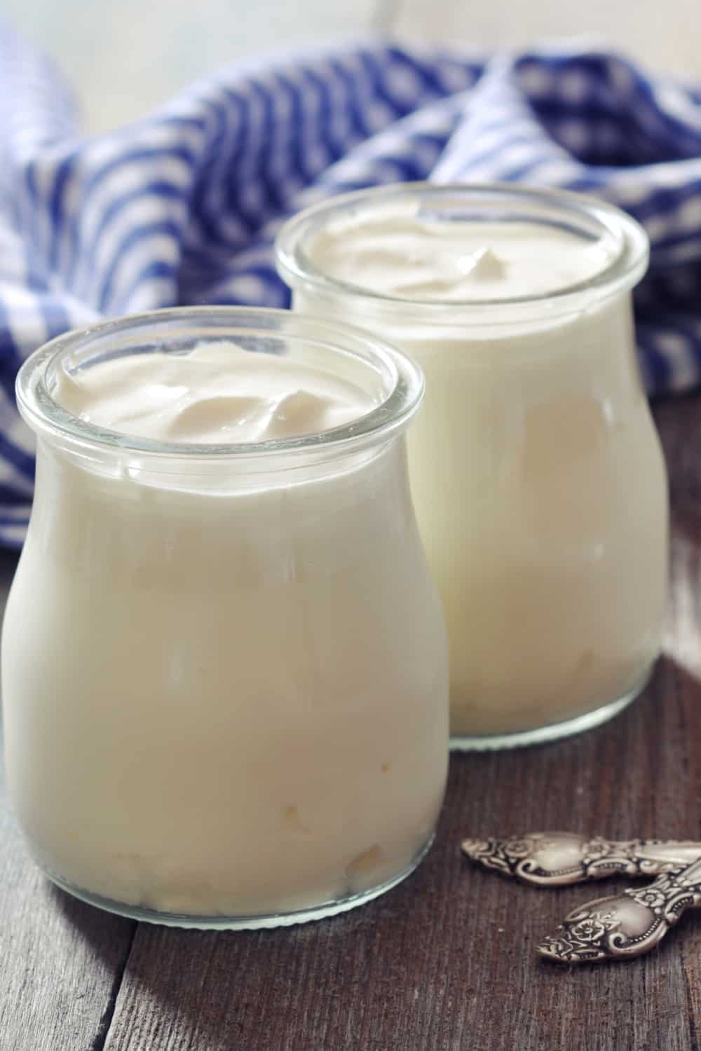 Yogur griego en tarros de cristal con cucharas sobre fondo de madera