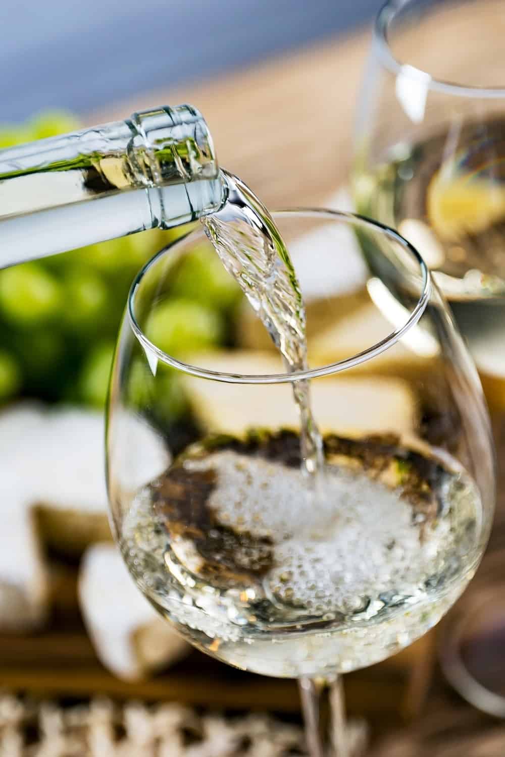 Pouring white wine into the glass against wooden table