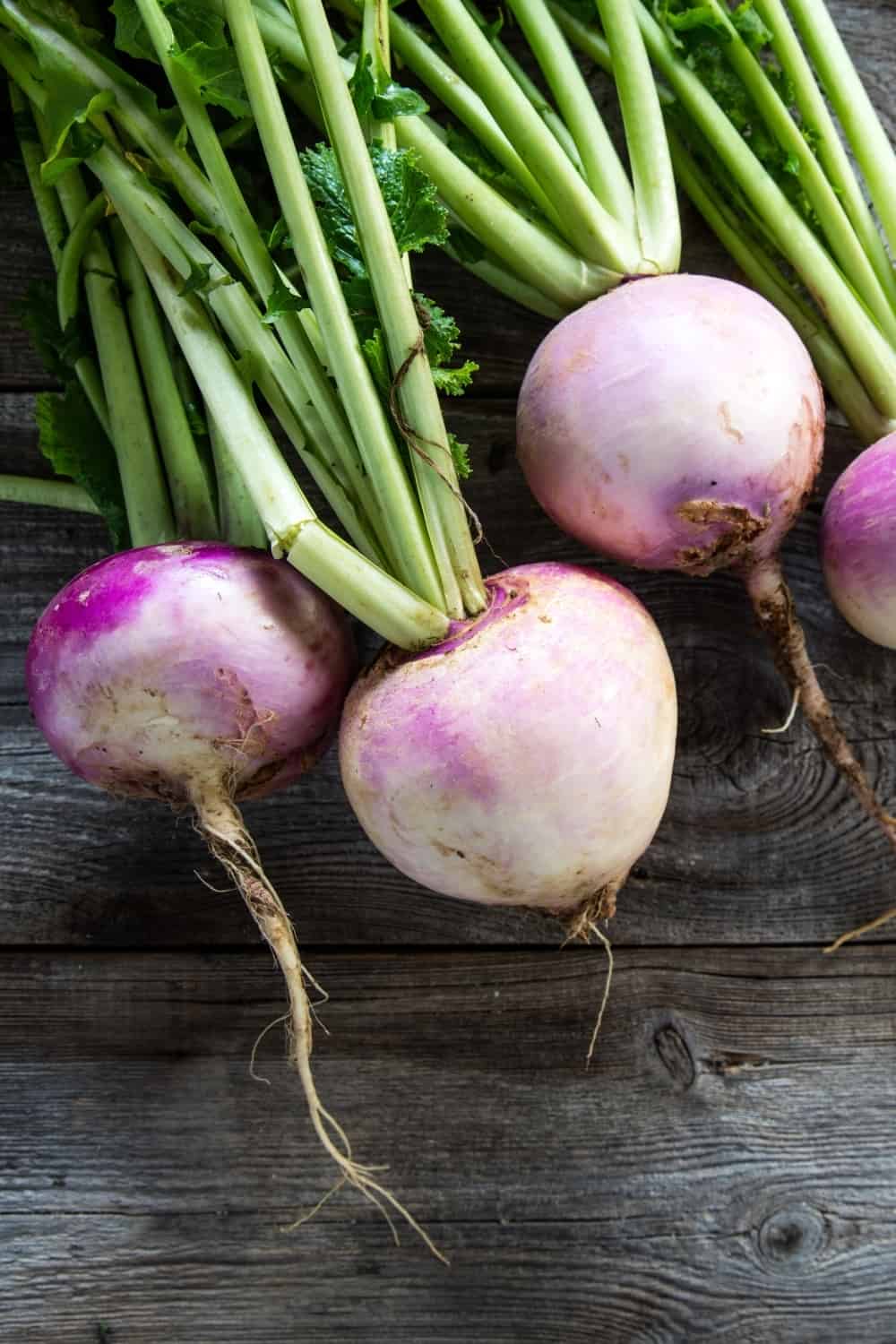 nabos rústicos orgánicos con tapas verdes frescas y raíces sobre fondo de madera genuina