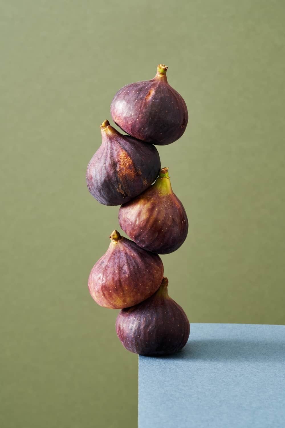 Fresh figs balancing on the edge of a table, with green background