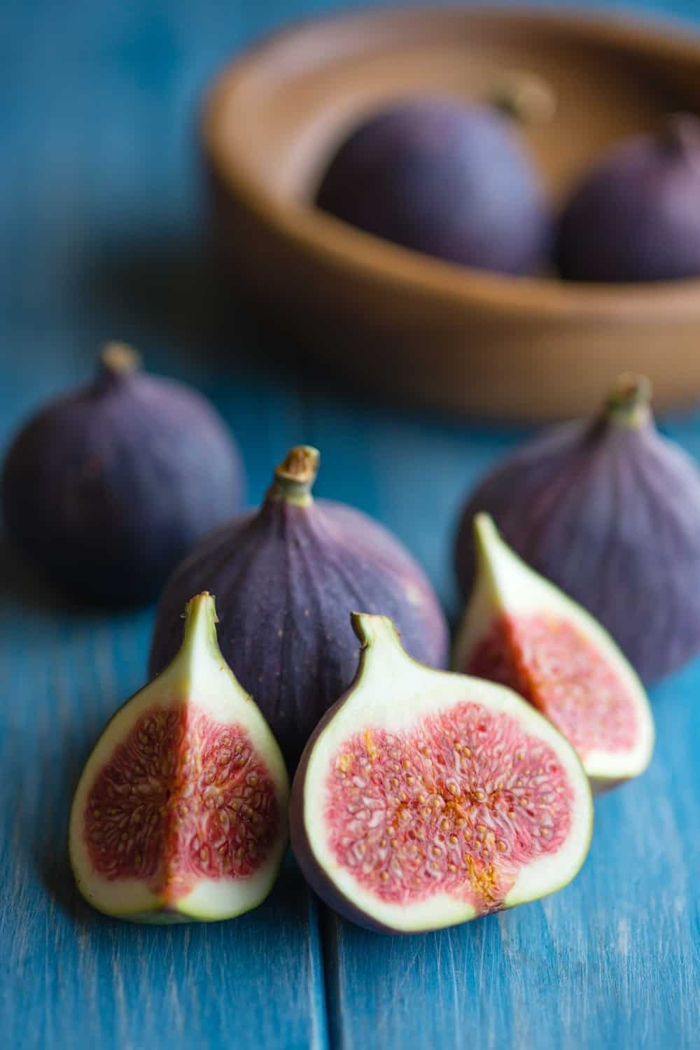 Group of figs in a bowl and on rustic blue wooden table