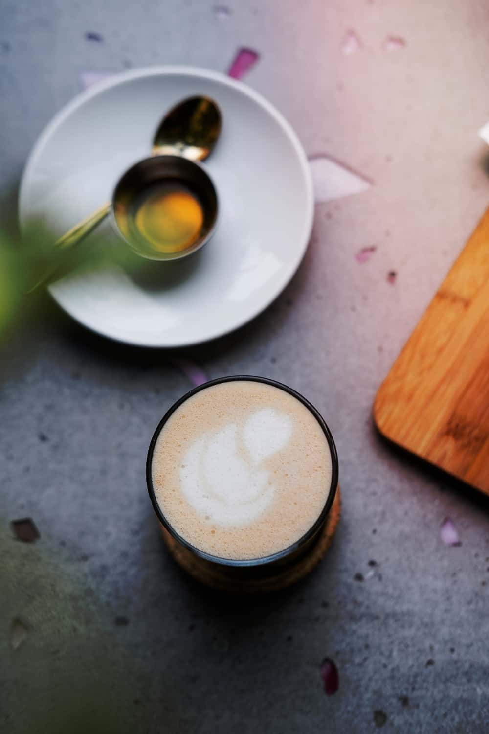 Masala chai latte con miel y caramelo vegano desde arriba sobre mesa de hormigón gris claro.