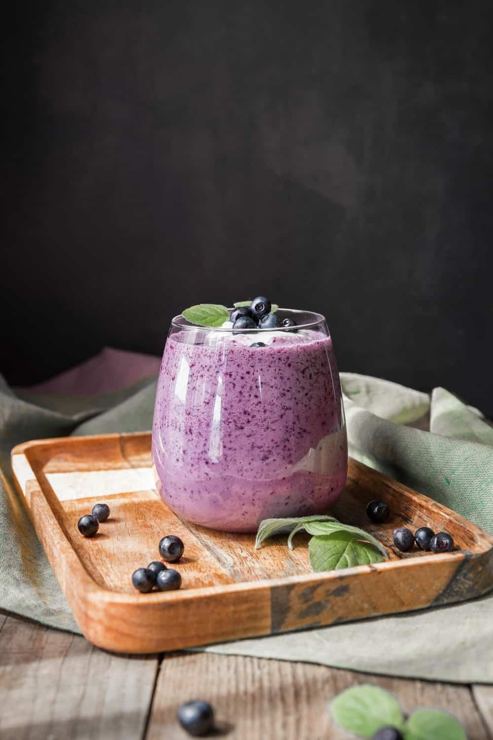 Blaubeer-Smoothie auf einem hölzernen Salver und schwarzem Hintergrund