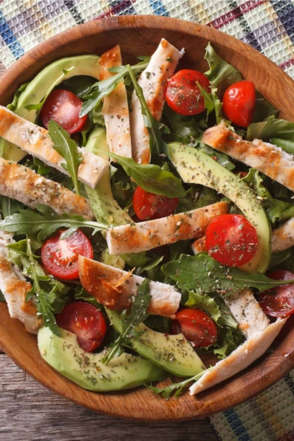 Hähnchensalat mit Avocado, Rucola und Kirschtomaten auf einem Holzteller