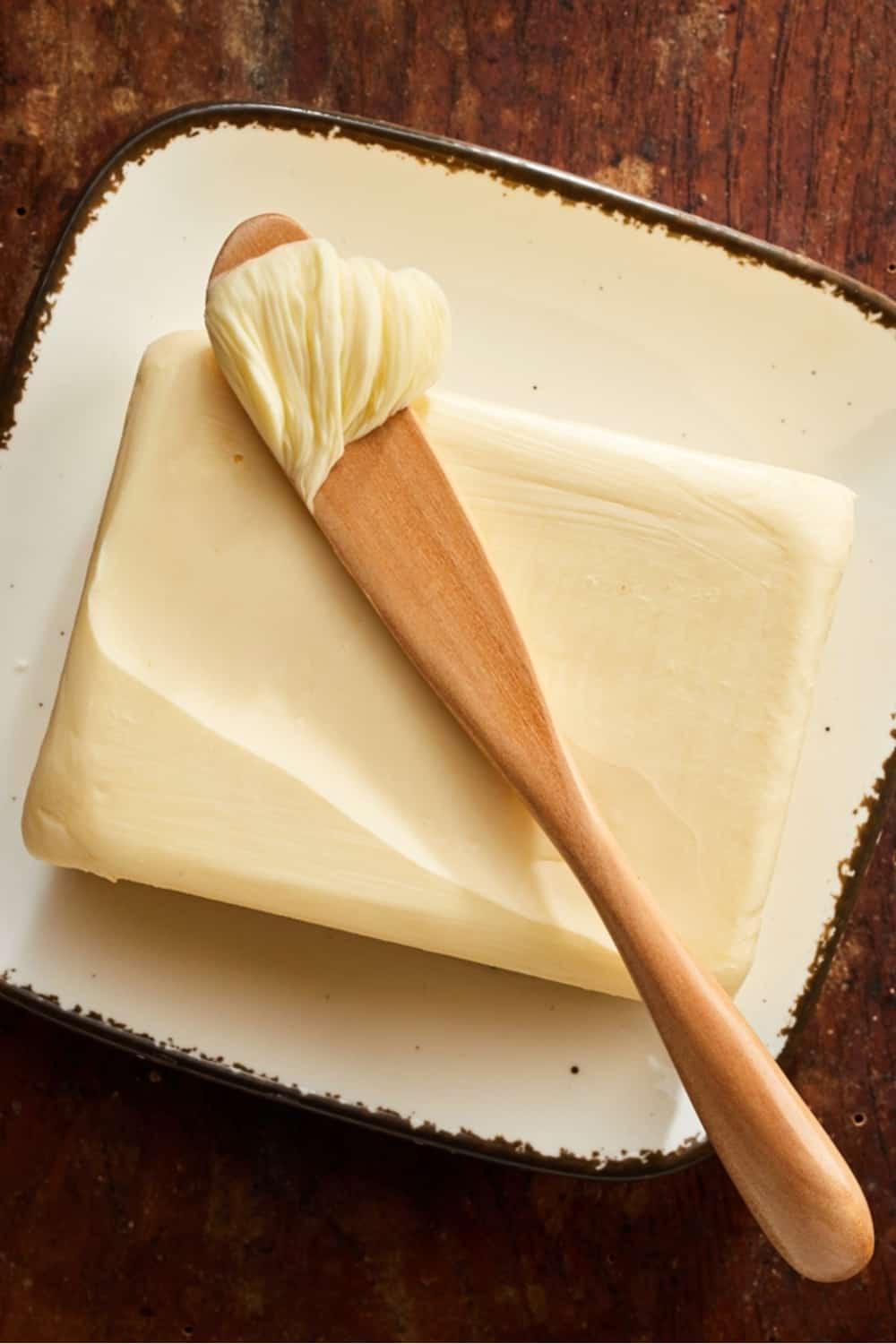 Pat de mantequilla de granja con esparcidor de madera con una cucharada de mantequilla