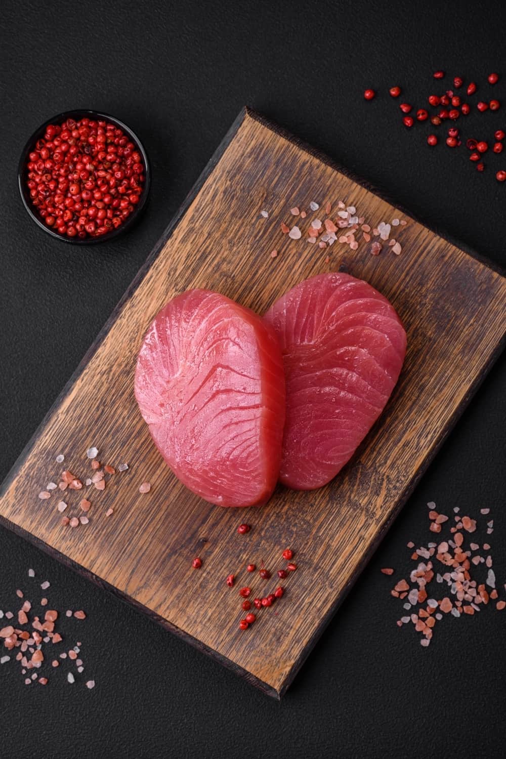 Two fresh slices of raw tuna fillet with spices and herbs on a dark concrete background