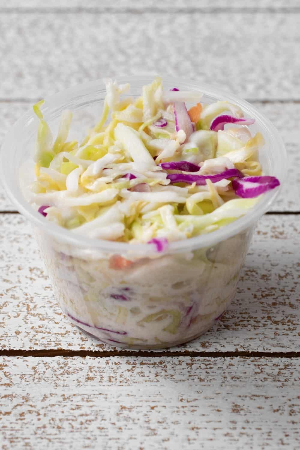 A view of a small plastic condiment cup of cole slaw.