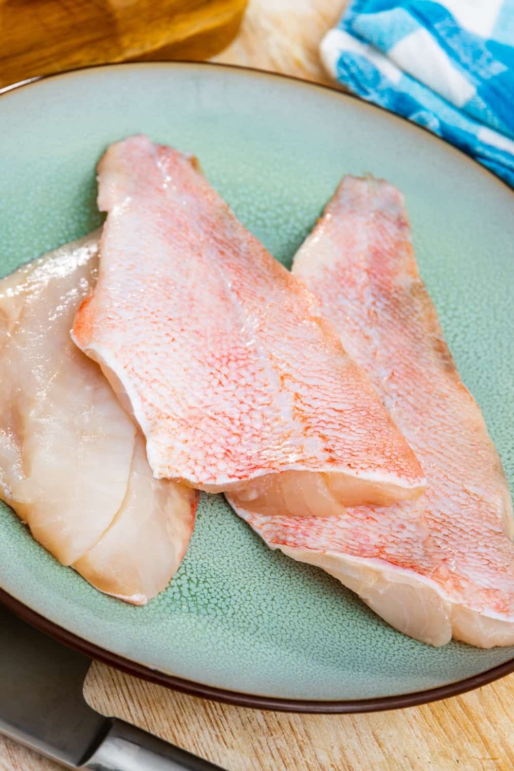 Filete de pescado de roca fresco crudo en plato con hierbas aromáticas y ajo sobre mesa de madera