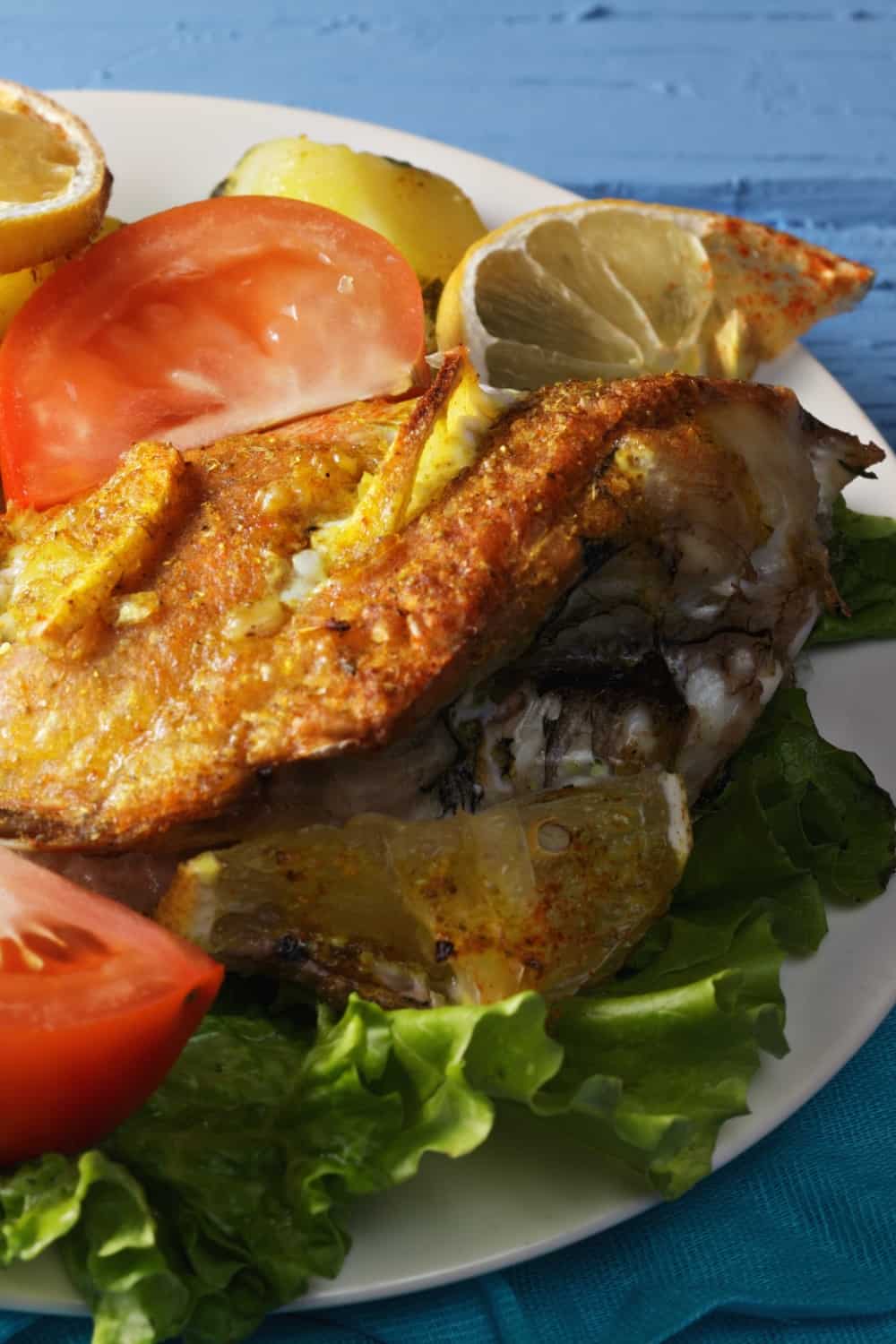 Peixe-pedra assado no forno com batatas e tomates sobre uma mesa de madeira